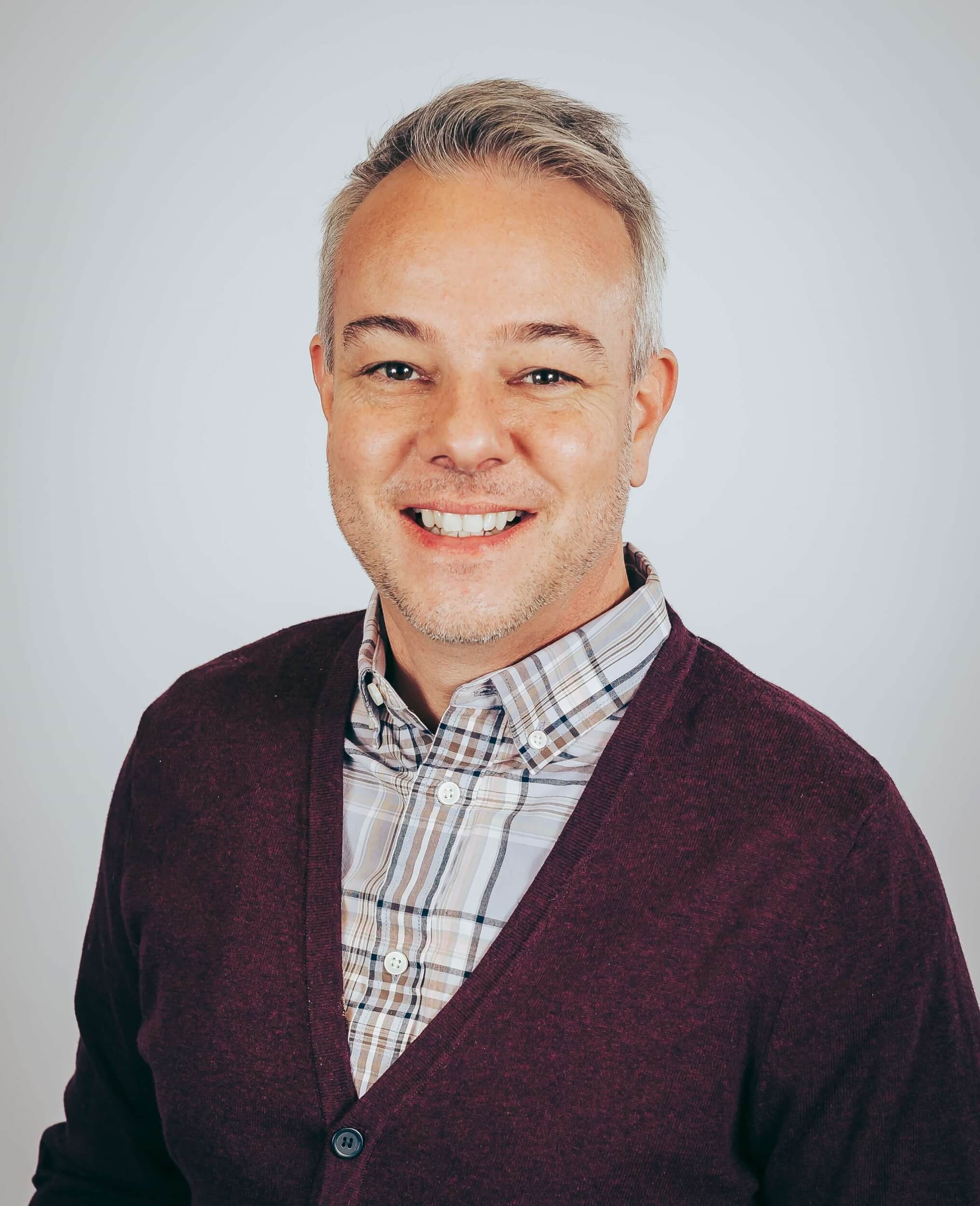 Dr. Robert Jason Grant wearing a plaid button up shirt and maroon cardigan