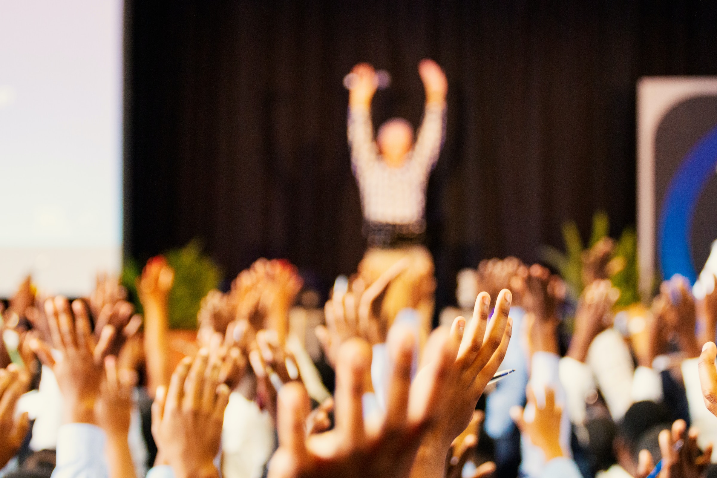 Workshop audience raising their hands with the speaker at the front with boht hands raised